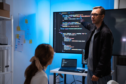 Software developers discussing code on large screen in office