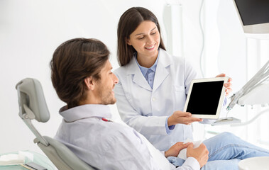 Obraz premium Woman dentist doctor showing patient empty digital tablet screen, modern technologies in healthcare