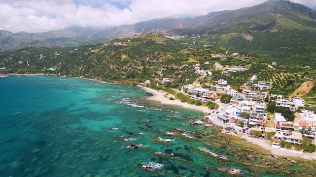 Plakias South Crete Greece aerial reveal of authentic white village, green hills and dramatic mountains with clouds, turquoise Mediterranean sea coastal landscape, traditional Greek island houses