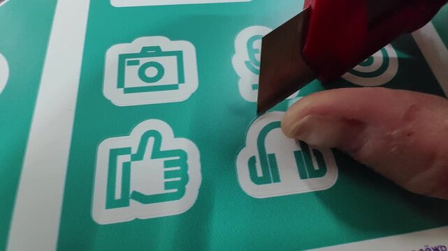 A hand with a stationery knife cuts out stickers