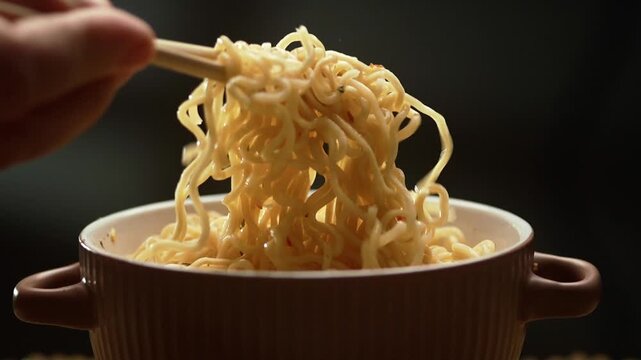 Eating instant noodles with chopsticks from bowl with smoke on black background. Healthy eating concept. Asian fast food