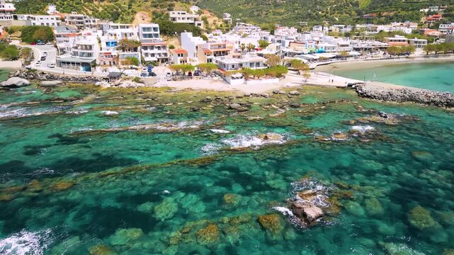 Aerial view of Plakias coastal village in South Crete, Greece. Drone low flight over turquoise transparent sea with camera tilt up to reveal white houses and majestic double mountains. 4k stock video.