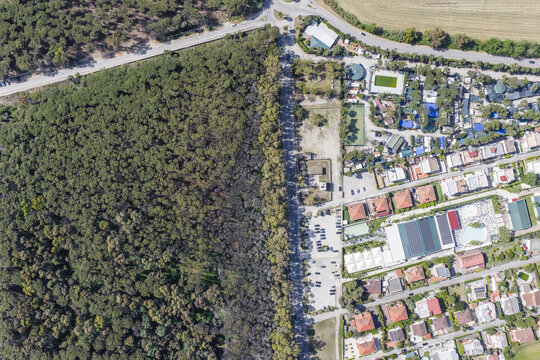 Aerial view of the sharp contrast between a dense green pine forest and a residential area with houses and swimming pools in Paestum, Campania, Italy.