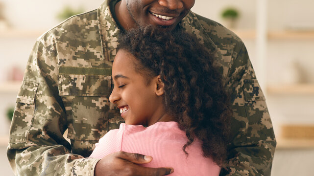 A soldier holds his daughter in a warm embrace as they reunite at a family gathering. The moment captures joy and love in a comfortable living space with soft lighting.