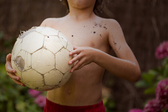 Close-up of a shirtless Boy with mud on his chest holding an old  football