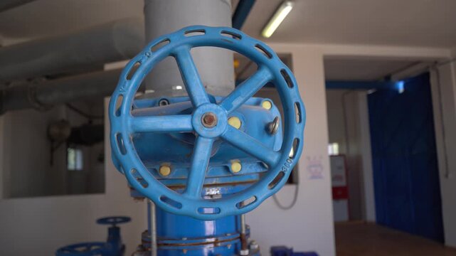 Smooth push-in shot of a large blue industrial valve wheel inside a modern pumping station. Ideal B-roll for projects focusing on water management, fluid control, infrastructure, and heavy industry.