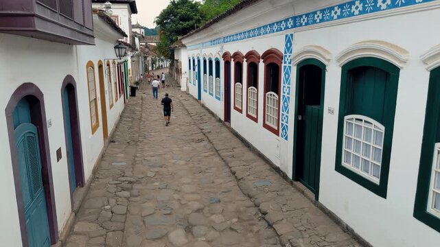 Street level view of colonial cobblestone street with colorful buildings, decorative patterns and tourists walking in UNESCO World Heritage Site historic center of Paraty, Brazil. Static camera