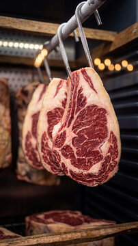 High-quality ribeye beef steaks hanging on metal hooks in a professional dry-aging refrigerator. Marbled raw meat, gourmet food storage, butcher shop.