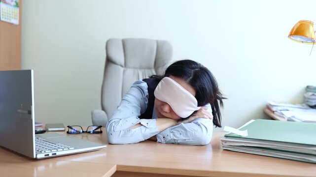 Business woman in a mask blindfolded asleep in the office. Exhausted employee in the workplace