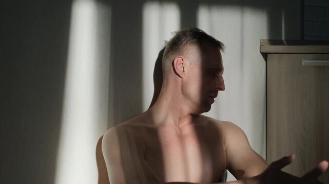 A frustrated sad man sits at home leaning against the wall in the evening