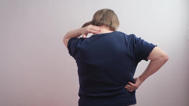 An elderly woman stretches her neck and back, feeling pain and discomfort.