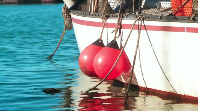 Red marina buoys floating beside fishing boat on calm harbor water, illustrating nautical transport, maritime safety and peaceful coastal atmosphere.