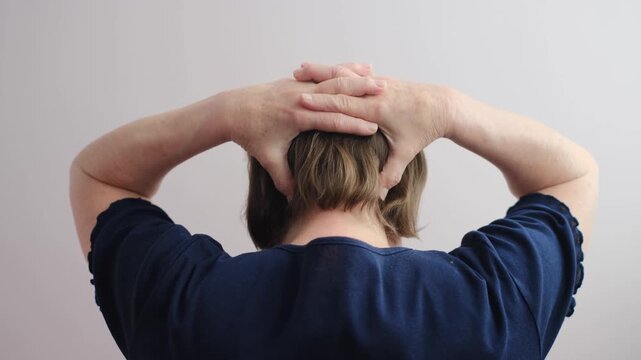 An elderly woman stretches her tired, sore neck from behind, close-up