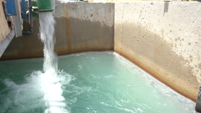 Water pours from a large green industrial pipe into a concrete basin filled with churning turquoise water. Ideal B-roll for water treatment, desalination, and industrial infrastructure projects.