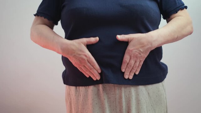 A woman rubs her stomach with her hands, feeling discomfort, close-up
