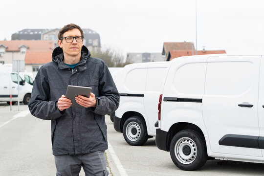 Fleet manager with digital tablet supervising rows of white delivery vans
