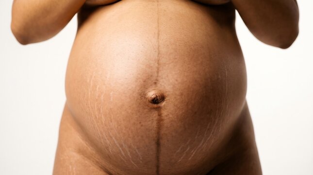 Professional close-up photograph of full term pregnant abdomen with realistic skin texture under golden studio lighting. Natural stretch marks and skin tone detail. Suitable for maternity healthcare c