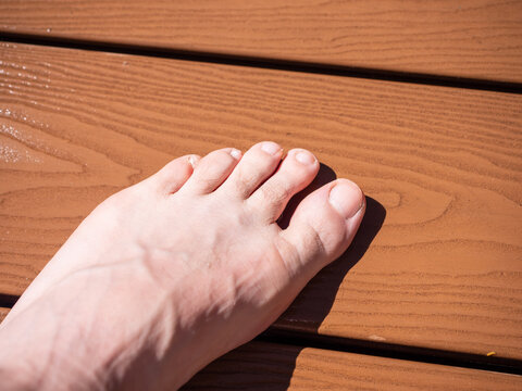 Bare foot on WPC decking near garden or pool. Closeup of modern composite terrace boards suitable for outdoor living, wellness and exterior design themes.
