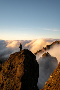lone hiker standing atop rocky mountain peak above clouds at sunrise enjoying serenity