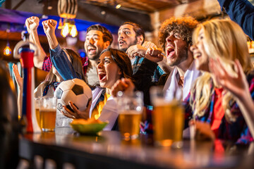 Excited group of friends holding soccer ball and cheering for goal in pub. © Mediteraneo