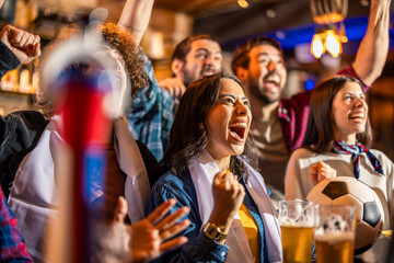Diverse group of friends watching soccer match and cheering together in urban pub. © Mediteraneo