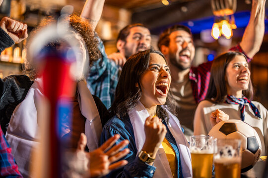 Diverse group of friends watching soccer match and cheering together in urban pub.
