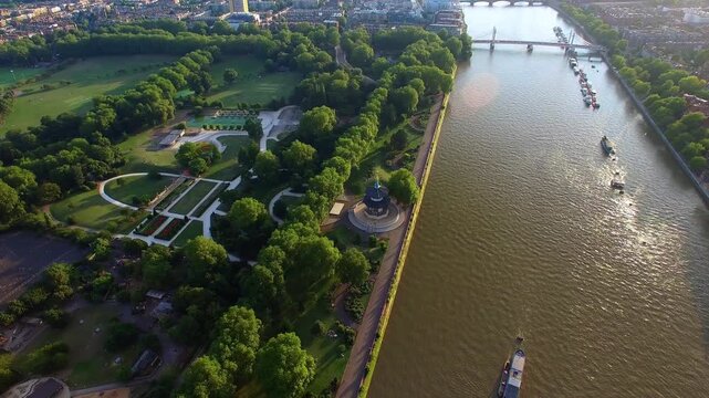 4K aerial view of Battersea Park with London Peace Pagoda, formal gardens, Albert Bridge, River Thames and Chelsea Embankment houseboats at golden hour summer evening.