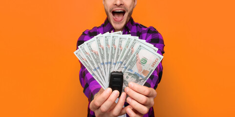 A person stands in front of an orange wall with a happy expression. They hold several bills in one hand and car keys in the other hand, showing excitement about money and a car. © Prostock-studio
