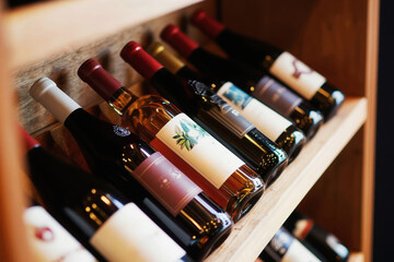 Obraz premium Assorted wine bottles rest on a wooden shelf in a cellar. Variety of red and white wines are stored neatly in a row for tasting or sale. Collection of premium alcoholic beverages.