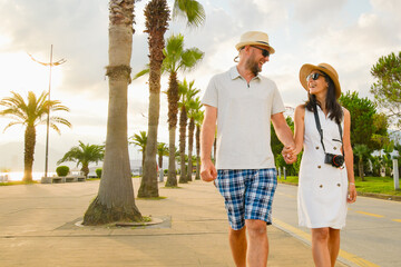Young couple tourists walking hand in hand along Batumi promenade with palm trees and seaside view on sunrise, concept of tourism, vacation, lifestyle and romantic travel in Georgia © Evaldas