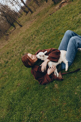 Fototapeta premium Woman lying on grass in a park, cuddling a white goat kid, enjoying a relaxed outdoor moment, soft light, natural colors, casual outfit, tranquil lifestyle scene