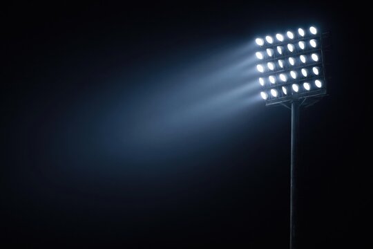 Powerful LED floodlight panel casting bright beam of light into dark night sky on stadium pole. High quality photo