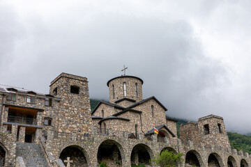 Obraz premium Exterior view of Alansky Holy Dormition Monastery stone church with bell tower and arches under low clouds in the Caucasus Mountains, North Ossetia-Alania, Russia