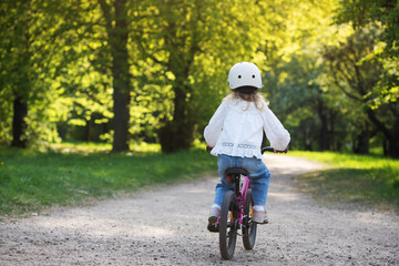 Fototapeta premium Little girl in cycling helmet enjoying riding bicycle in nature outdoor, toddler active leisure, happy bike ride on park trail in sunlight.