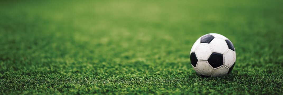 Traditional black and white soccer ball placed on vibrant green lawn of sports field with shallow depth of field. High quality photo