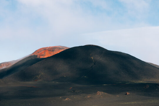 Volcanic cinder cone and black ash desert in Tolbachinsky Dol, Kamchatka Krai, Russia, with red scoria slopes and wide barren terrain under a cloudy sky