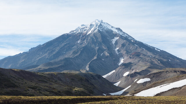 Scenic view of Koryaksky Sopka stratovolcano with snowfields on rocky slopes under a cloudy sky in Kamchatka Krai, Russia, remote volcanic wilderness