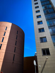 Fototapeta premium Contemporary cityscape featuring high-rise residential buildings with mixed architectural styles under clear blue sky. Combination of geometric towers and curved facade