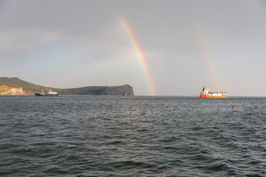 Wide seascape with cargo ships and a double rainbow over Avacha Bay near Petropavlovsk-Kamchatsky, Kamchatka Krai, Russia, with cliffs and calm water