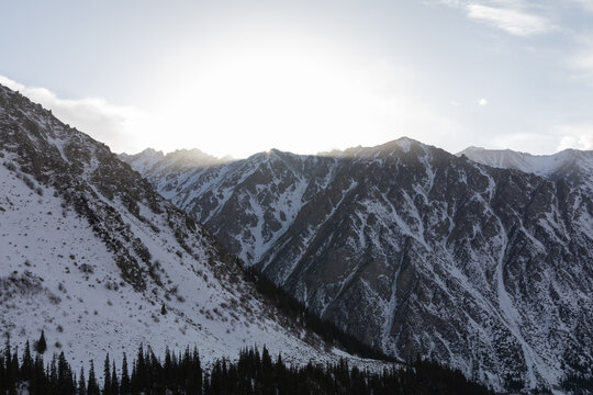Scenic winter view of snow-covered mountains and dark conifer forest at sunrise in Ala Archa National Park near Bishkek, Chuy Region, Kyrgyzstan