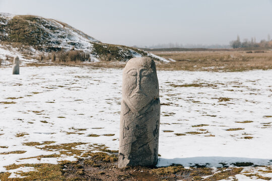 Weathered stone balbal statue standing in a snowy steppe field at the Burana Tower archaeological complex near Tokmok, Kyrgyzstan