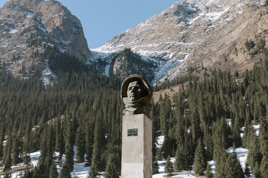 Monument to cosmonaut Yuri Gagarin in Barskoon Gorge, Issyk-Kul Region, Kyrgyzstan, set against pine forest slopes and snowcapped Tien Shan peaks