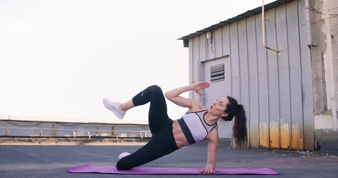 Plank exercise. Kneeling fitness. Athletic woman on rooftop performing physical lifting leg focusing on oblique hip abductor strength.