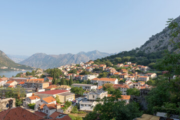 Fototapeta premium Wide panoramic view over Kotor with red tiled rooftops, green hills and rugged mountains above the Bay of Kotor, Montenegro, on a clear sunny day