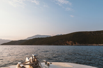 View from the bow of a small boat cruising on calm sea toward green coastal hills and distant mountains at sunset, with clear sky and copy space for travel themes © TravelFlow