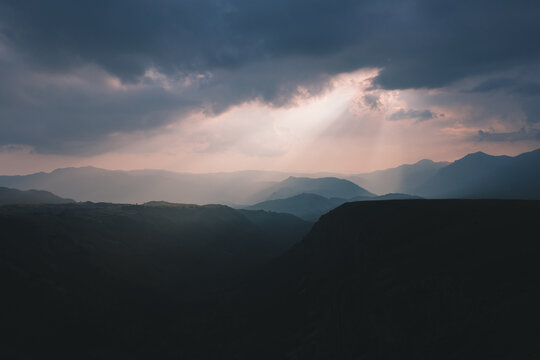 Wide landscape view of layered mountain ridges and a deep canyon at sunset in Durmitor National Park, Montenegro, with sun rays breaking through dark storm clouds