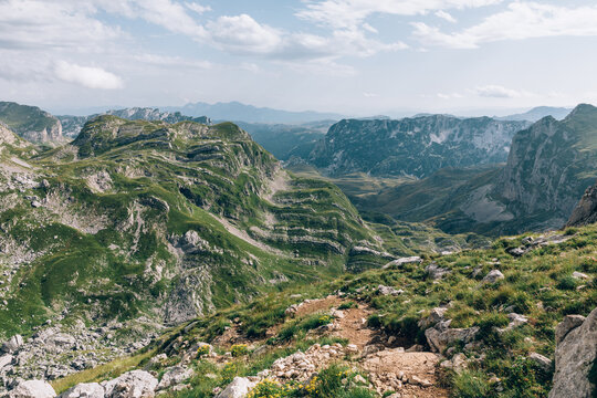 Panoramic view of rugged limestone peaks, green alpine meadows and a rocky hiking path near Bobotov Kuk in Durmitor National Park, Montenegro, on a sunny day