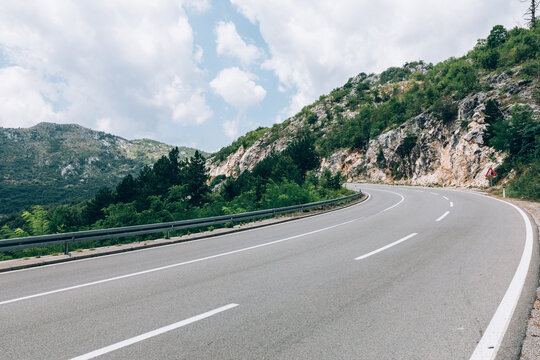 Empty winding asphalt highway through rugged mountains with guardrail and traffic sign under dramatic clouds, near Kotor, Kotor Municipality, Montenegro