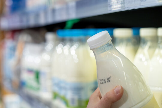 Womans hand holding milk bottle in supermarket. Man shopping milk in grocery store. Customer checks product expiration date before buying it. Close-up.
