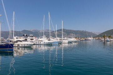 Fototapeta premium Panoramic view of luxury yachts and sailboats docked in Porto Montenegro marina, Tivat, Montenegro, with calm blue water reflections and mountains under clear sky